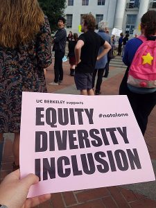 A hand holding a pink flyer that states UC Berkeley supports Equity, Diversity and Inclusion #notalone